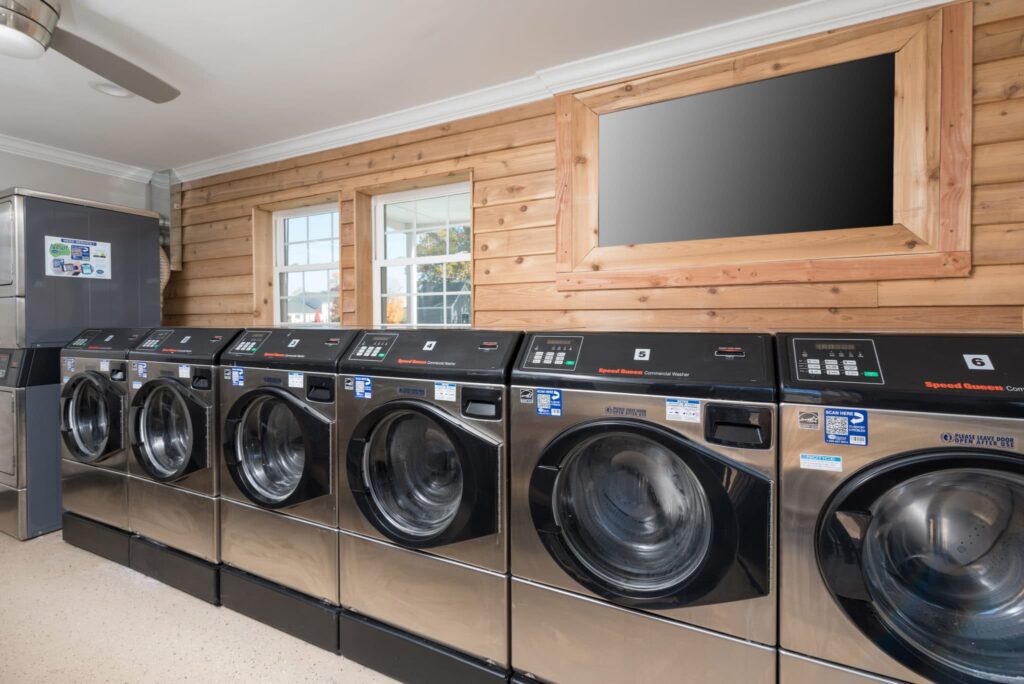 A row of six stainless steel washing machines in a laundromat with wooden walls and a blank mirror above reflects the understated elegance found in nearby luxury 2-bedroom apartments in Charlottesville. | Spark Living